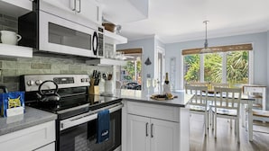 A modern kitchen with white cabinets, a black stove, and a dining area with a wooden table and chairs.