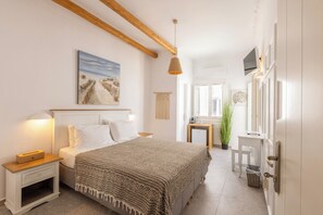 A bedroom with a bed, bedside tables, a hanging light fixture, a painting on the wall, and a view of the hallway. - Parosquare Central Suites (Paros)