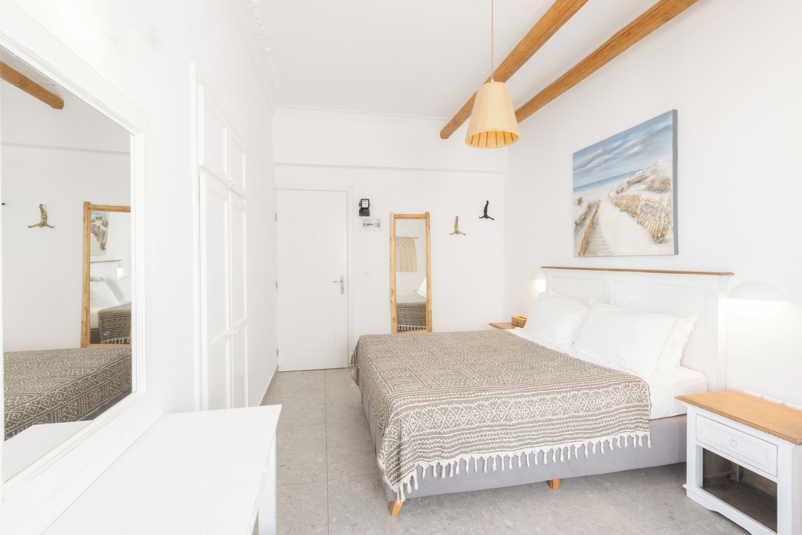 A bedroom with a bed, bedside table, nightstand, and a large mirror.