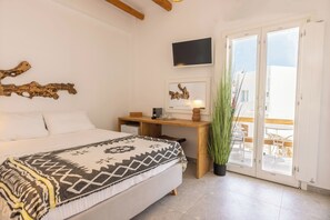 A bedroom with a bed, a desk, a TV, and a balcony with a view. - Parosquare Central Suites (Paros)