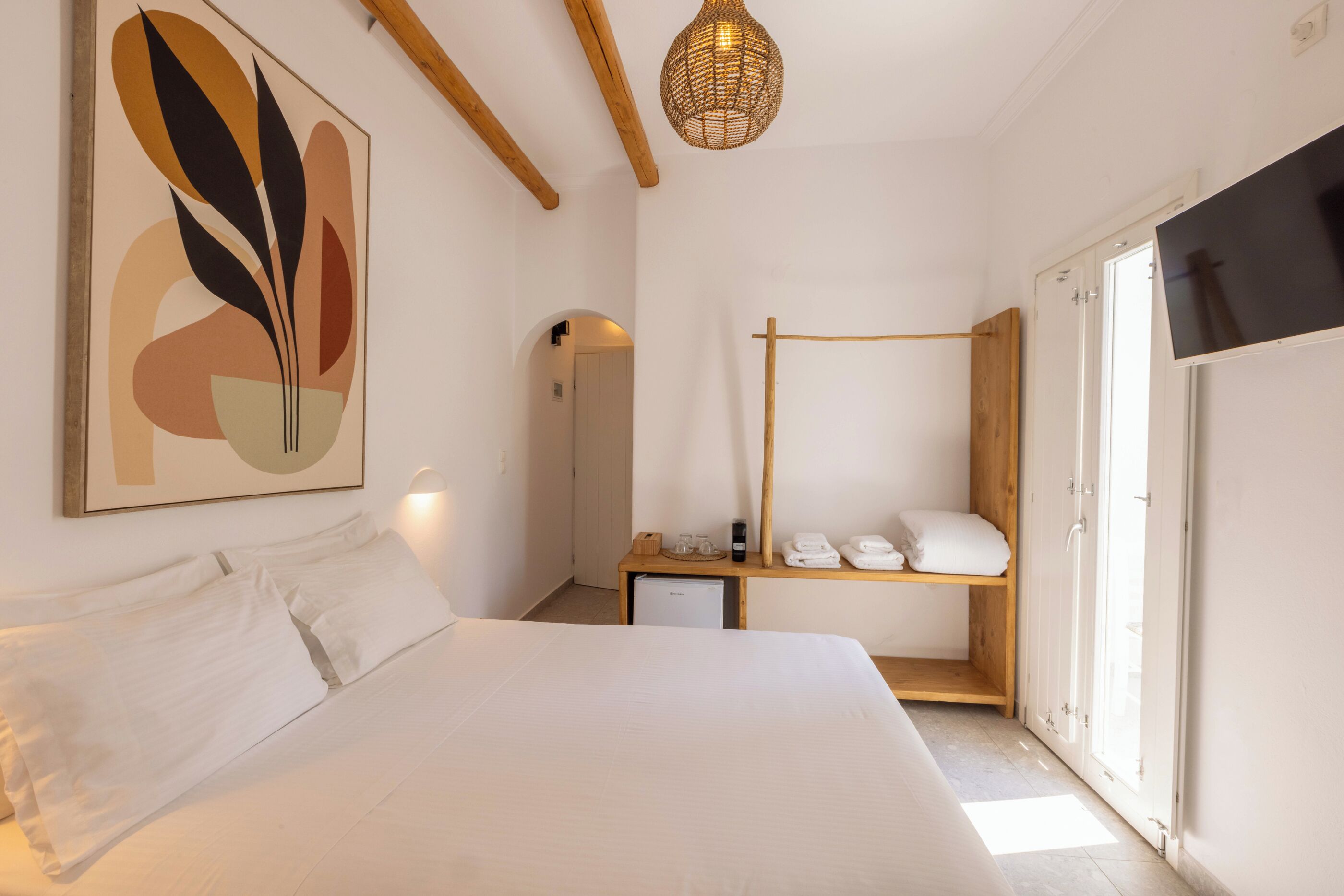 Una habitación de hotel moderna con una cama grande, una mesita de noche, un escritorio pequeño, un armario y un ventanal amplio.