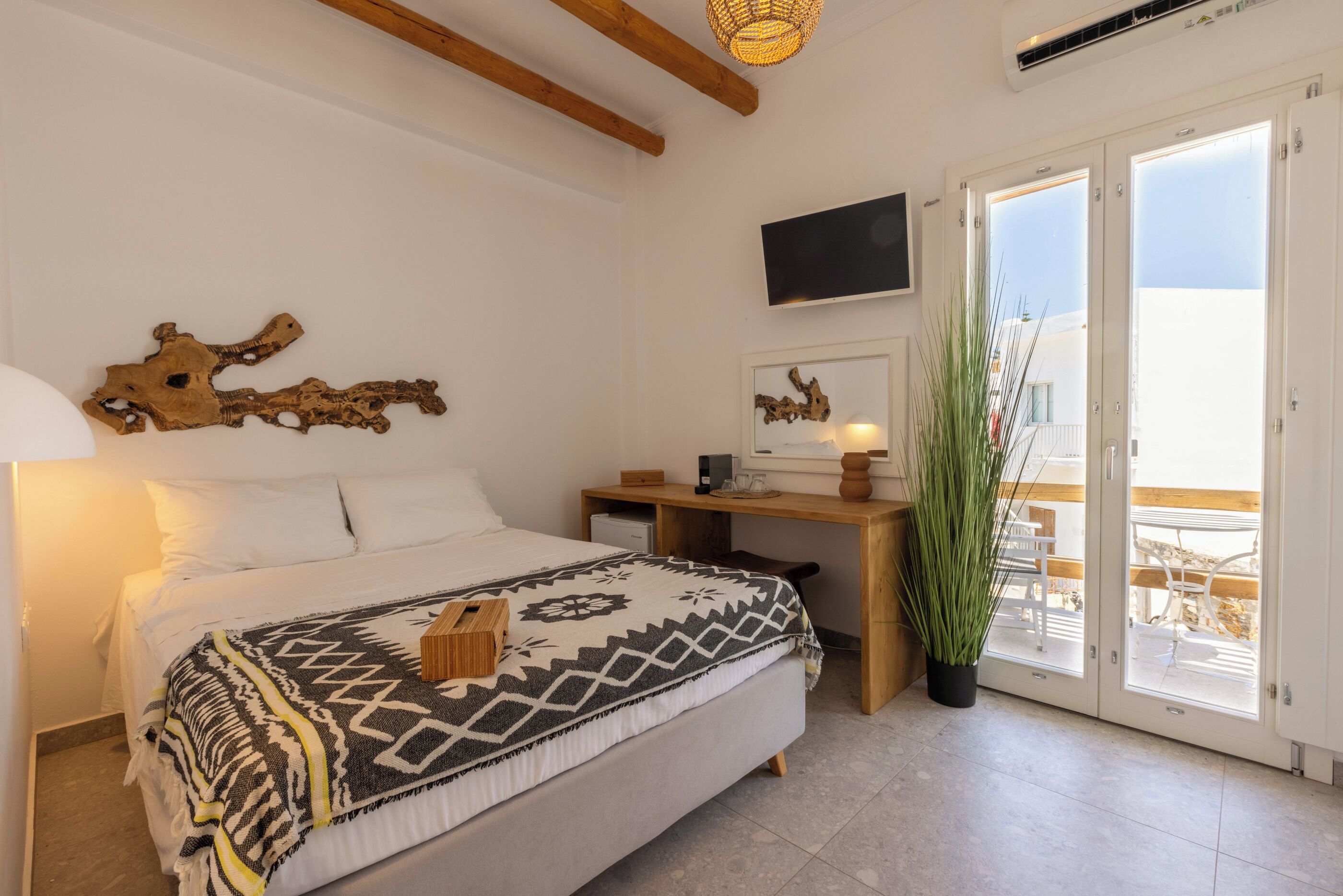 A bedroom with a bed, a desk, a television, and a balcony with a view.