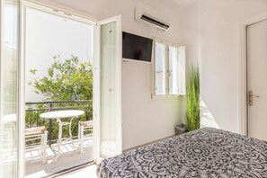 A bedroom with a bed, a window, a balcony with a table and chairs, and a potted plant. - Parosquare Central Suites (Paros)
