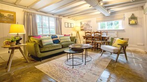 A cozy living room with a green sofa, a round coffee table, and a dining area with wooden chairs and a table. - Locke's Cottage - sleeps 2 guests  in 1 bedroom (Stratford-upon-Avon)