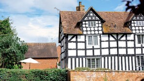 A traditional half-timbered house with a brick chimney, white and black timber framing, and a brick wall. - Locke's Cottage - sleeps 2 guests  in 1 bedroom (Stratford-upon-Avon)