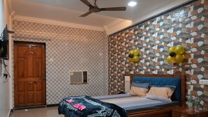 A bedroom with a checkered wall, a wooden door, a ceiling fan, a bed with a blue headboard, and decorative balloons. - Hotel Nakshtra, Shrungartali (Guhagar)
