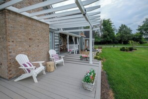 Un portico coperto con due poltrone Adirondack, uno sgabello di legno e un fioriera con fiori.