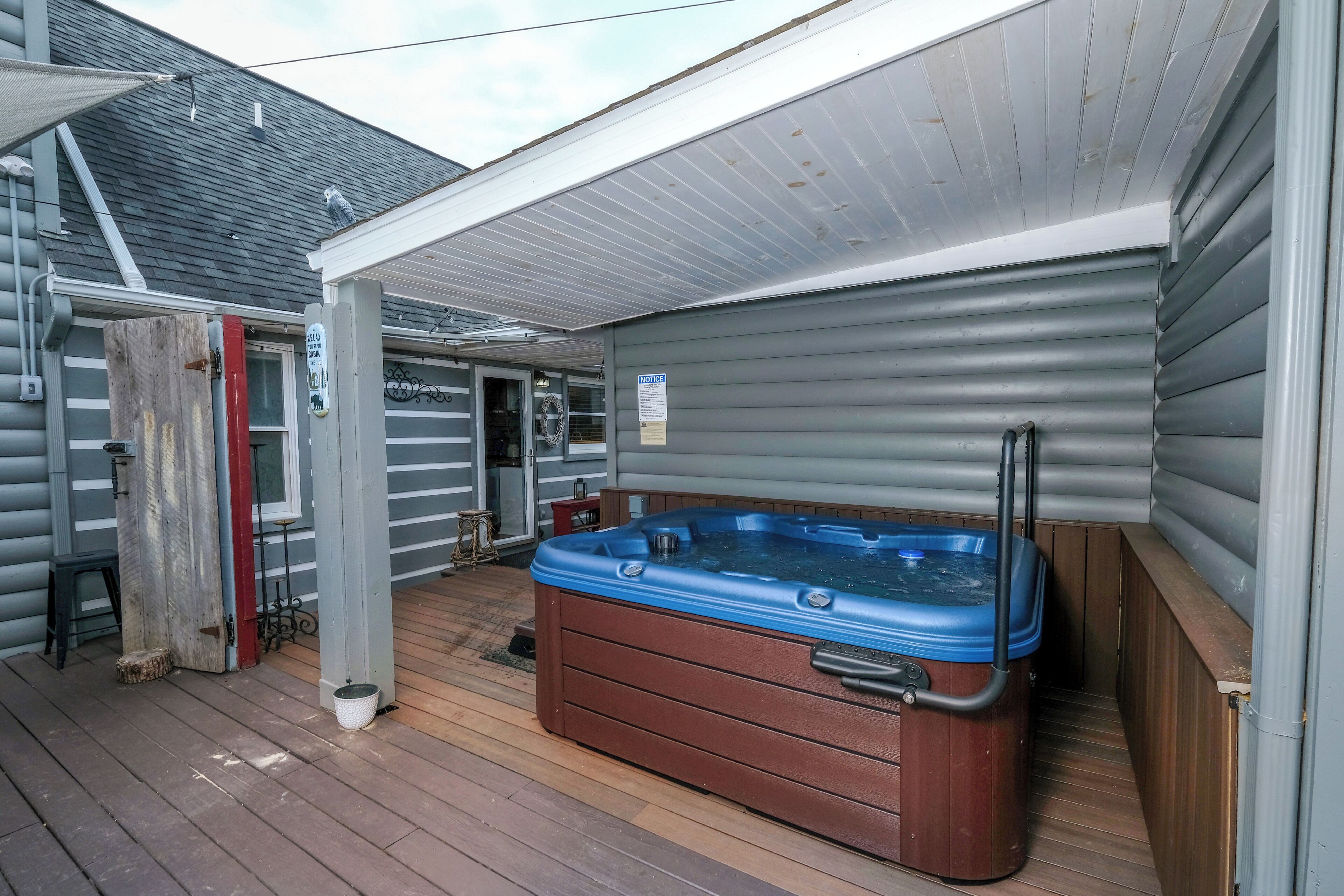 Ein Whirlpool auf einer Holzterrasse mit überdachter Veranda und Blick auf das Haus.