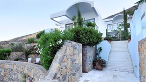 Un edificio moderno con un muro de piedra de contención, una escalera que conduce a una puerta blanca y vistas a una colina.