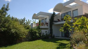 Una casa moderna de dos pisos con techo plano, ventanas amplias y un balcón.