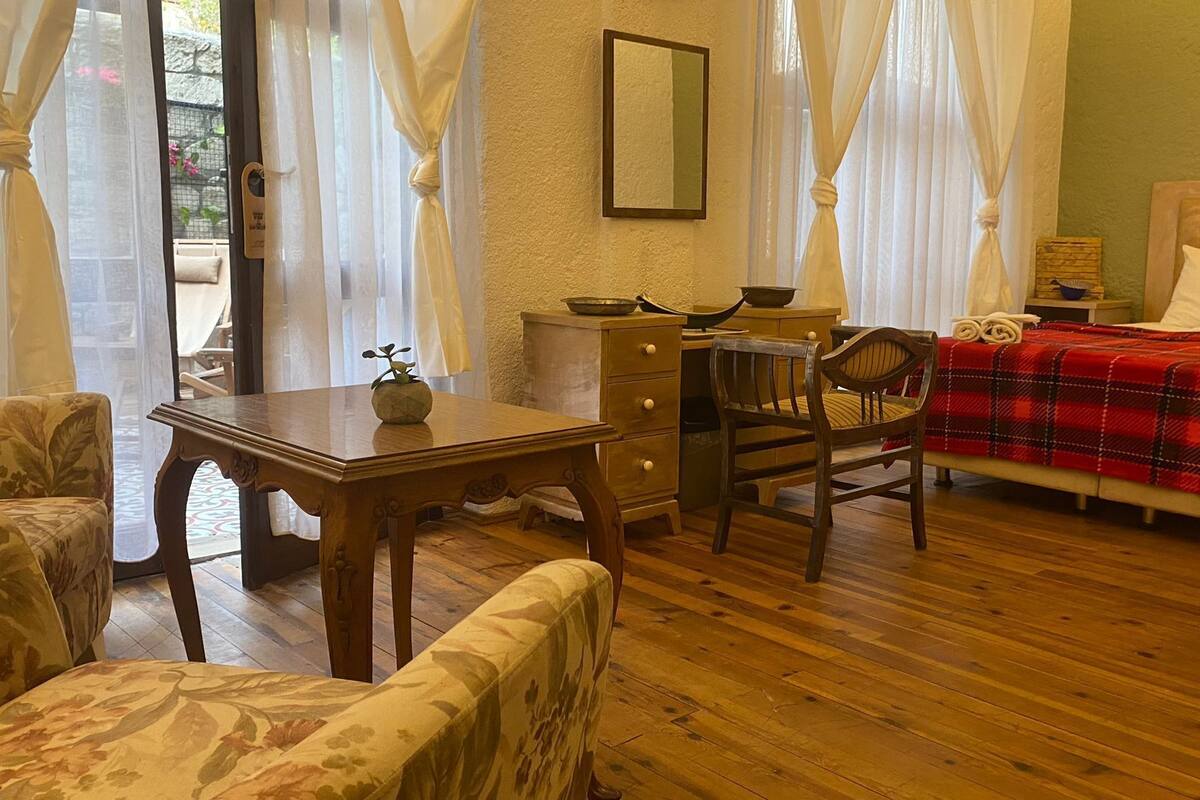 Ein gemütliches Zimmer mit einem Holztisch, einem Stuhl, einem Bett mit roter Decke und einem Nachttisch.