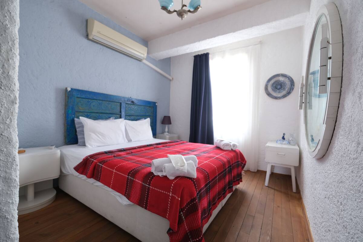 Ein Schlafzimmer mit Bett, Nachttisch, Spiegel und einem Fenster mit Vorhängen.
