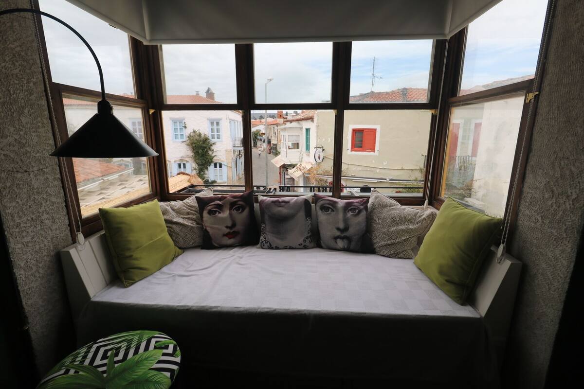 Eine gemütliche Leseecke mit Blick auf eine Stadtlandschaft durch große Fenster.