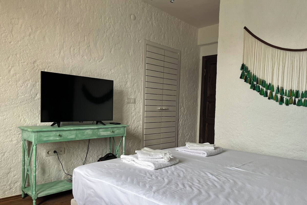 Ein Schlafzimmer mit einem Bett, einem Fernseher auf einer grünen Kommode, einem Kleiderschrank und einer Wanddekoration.