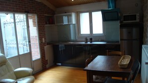 A compact kitchen with a dining area, featuring a wooden table, chairs, and a brick wall.