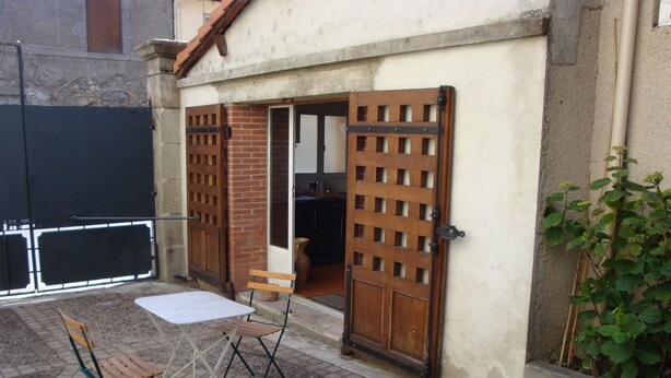 A patio with a table and chairs, a wooden gate, and a brick wall.