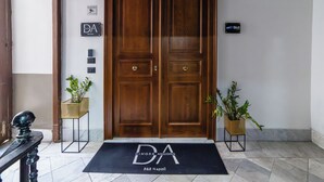 A double wooden door with a black mat in front, two potted plants, and a sign with 'DA' on the wall. - Dimora Angioina  (Naples)