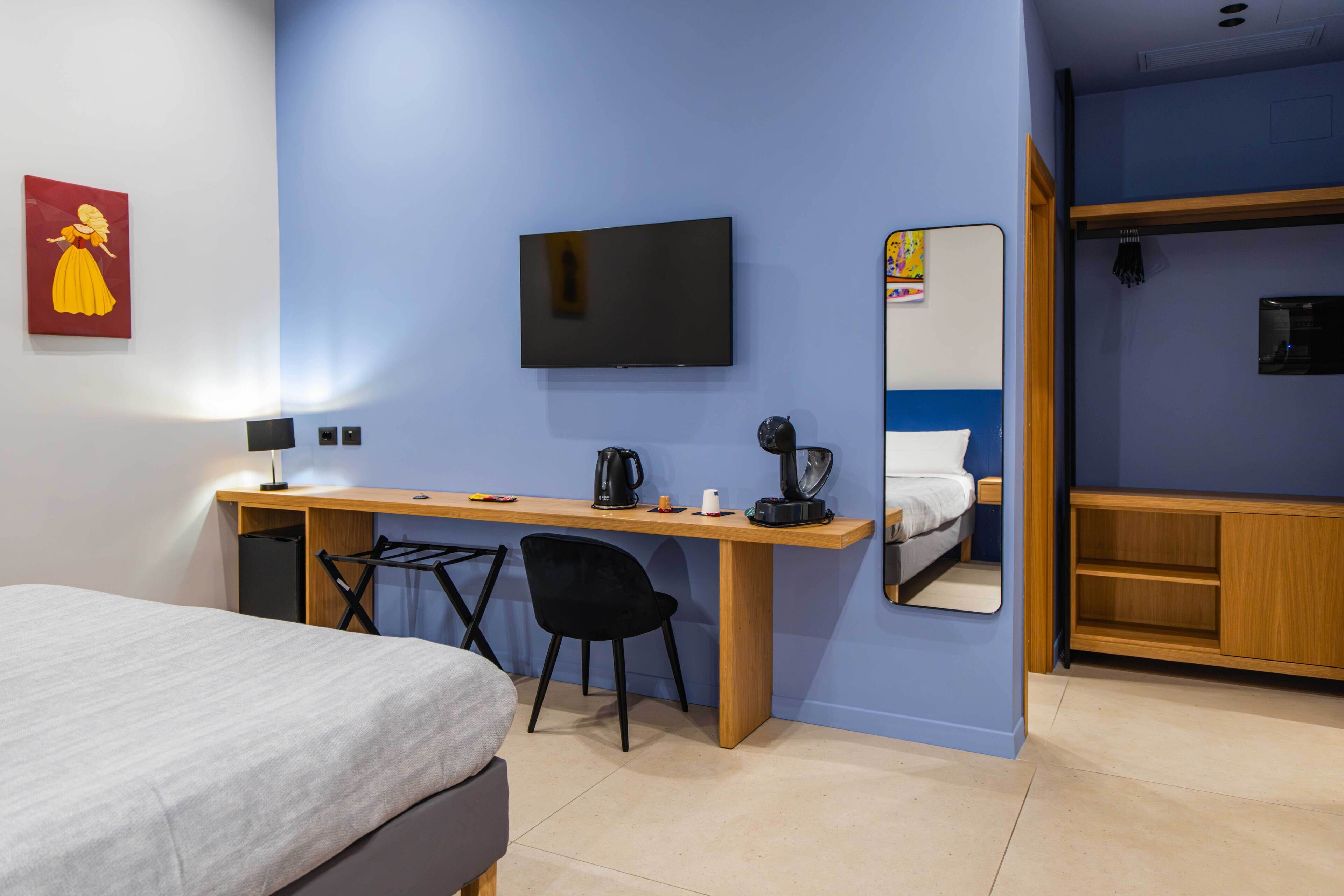 A hotel room with a bed, a desk with a chair, a television, a mirror, and a wardrobe.