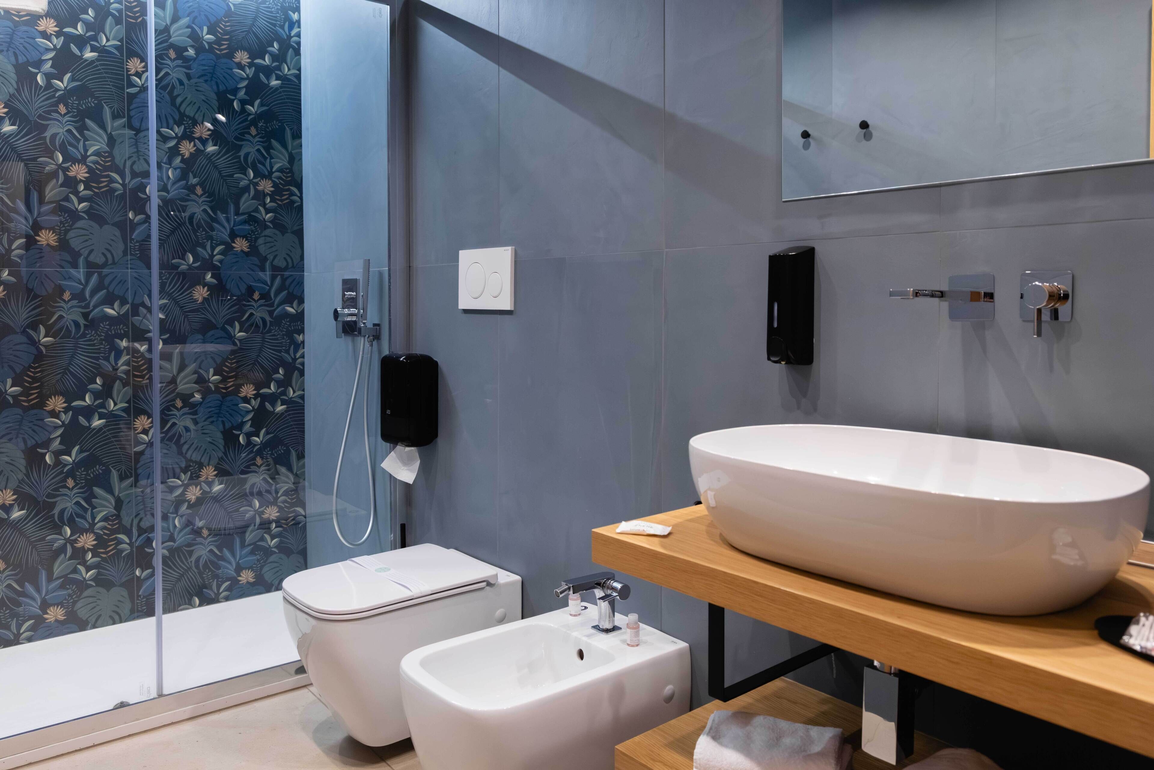 Une salle de bain moderne équipée d’un bidet, d’un grand lavabo blanc, d’un miroir et d’un espace douche avec une porte en verre.