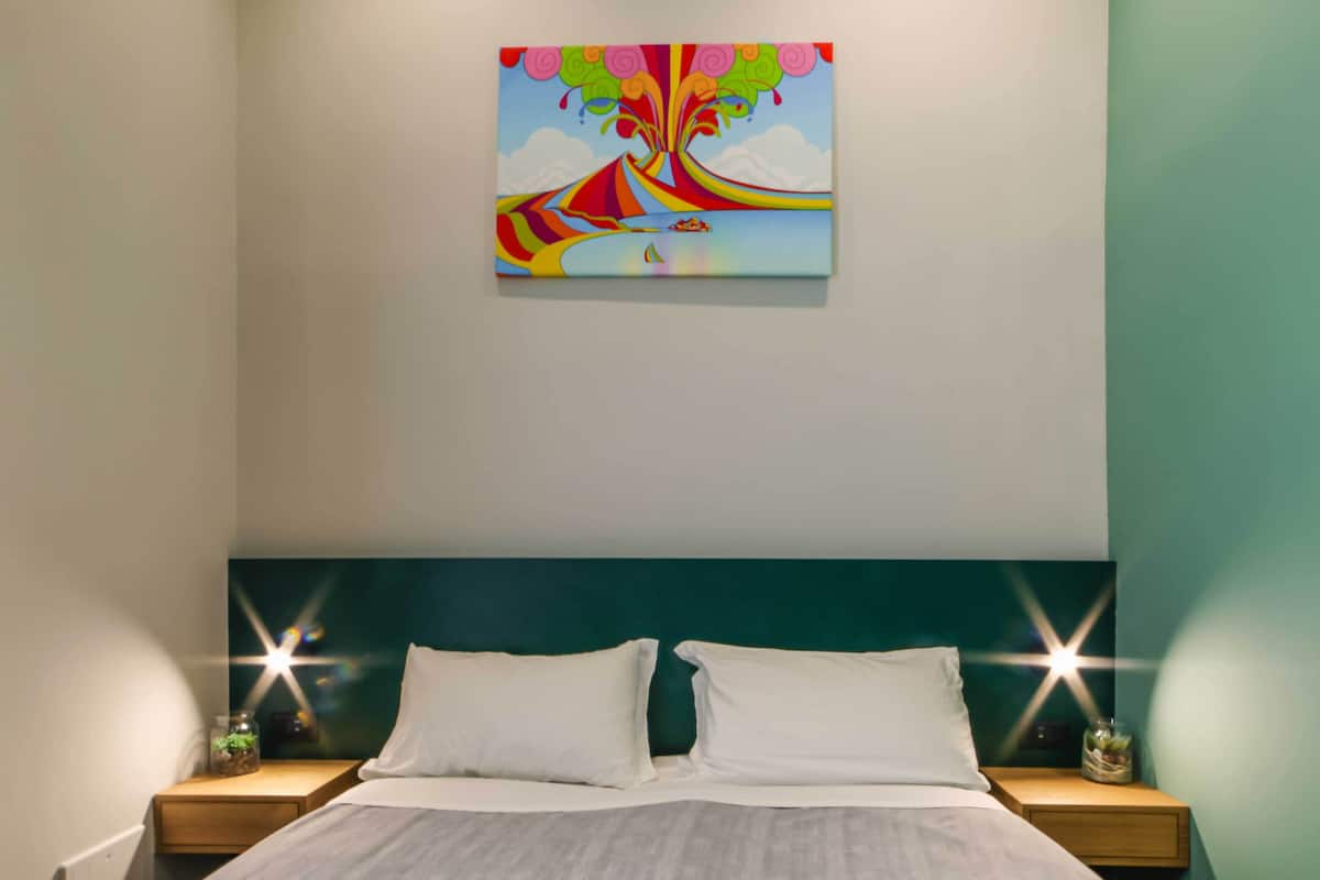 A bedroom with a bed, two bedside tables, a nightstand, a wall-mounted painting, and a star-shaped light fixture.