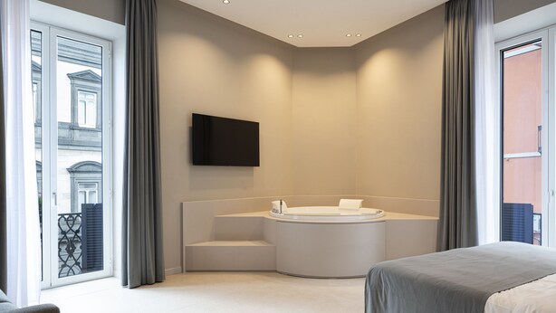 A modern hotel room with a large bed, a built-in bathtub, and a flat-screen TV mounted on the wall. - Dimora Angioina  (Naples)