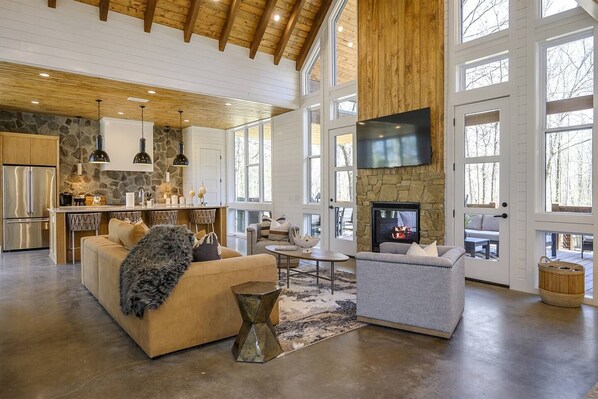 Un amplio salón con chimenea, una cocina con detalles de piedra y ventanas grandes.
