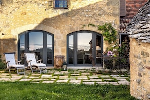 A stone building with large arched windows, outdoor seating, and a garden area. - Promo Dernière Minute Magnifique (Beynac-et-Cazenac)
