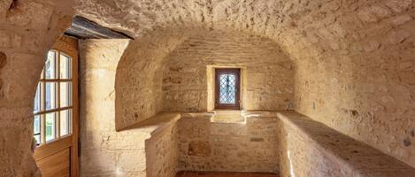 A stone-walled room with a wooden door, a small window, and a tiled floor.