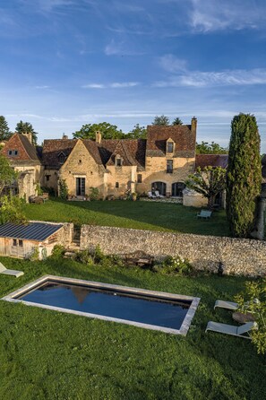 Ein Steinhaus mit Swimmingpool, umgeben von einer Rasenfläche und einer Steinmauer.