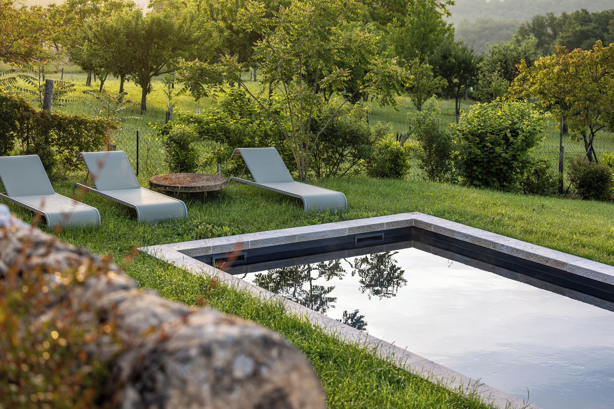 An outdoor swimming pool with lounge chairs and a stone table.