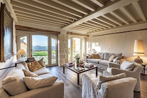 Een ruime woonkamer met een hoge plafond, grote ramen en uitzicht op het landschap.