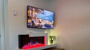 Una sala de estar con una televisión de pantalla plana sobre la chimenea, una mesita y una planta en maceta.