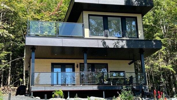 Una casa moderna de dos pisos con balcón, ventanas grandes y una terraza.