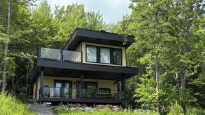 Una casa moderna de dos pisos con balcón, rodeada de un bosque.