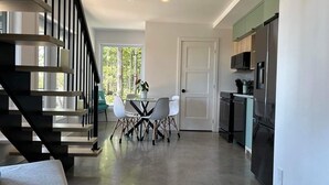 Una cocina moderna con comedor, una escalera y vistas al exterior con vegetación.
