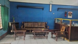 A room with a blue wall, a wooden sofa, two wooden chairs, a small table, a clock, and a shelf with items. - Hotel O Penginapan Keluarga (Medan)