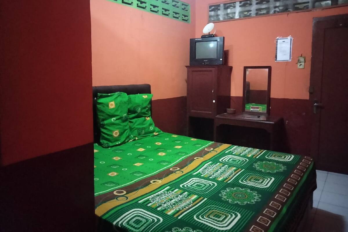 A bedroom with a bed, a television on a stand, a mirror, and a wardrobe.