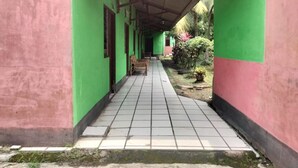 A corridor with green walls and a tiled floor, leading to a covered area with benches. - Hotel O Penginapan Keluarga (Medan)