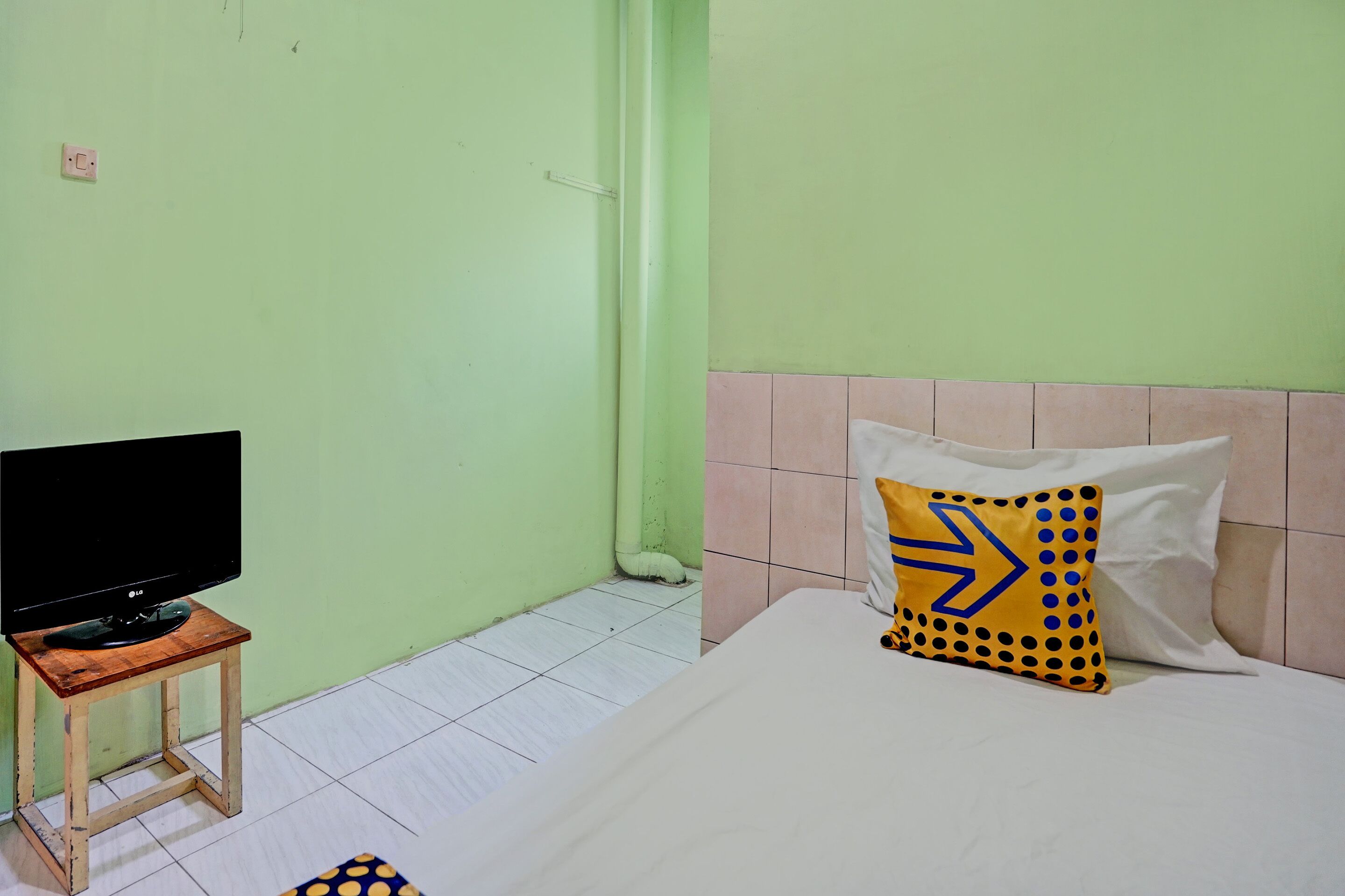 Une pièce avec un lit, un téléviseur posé sur une petite table en bois et un mur vert.