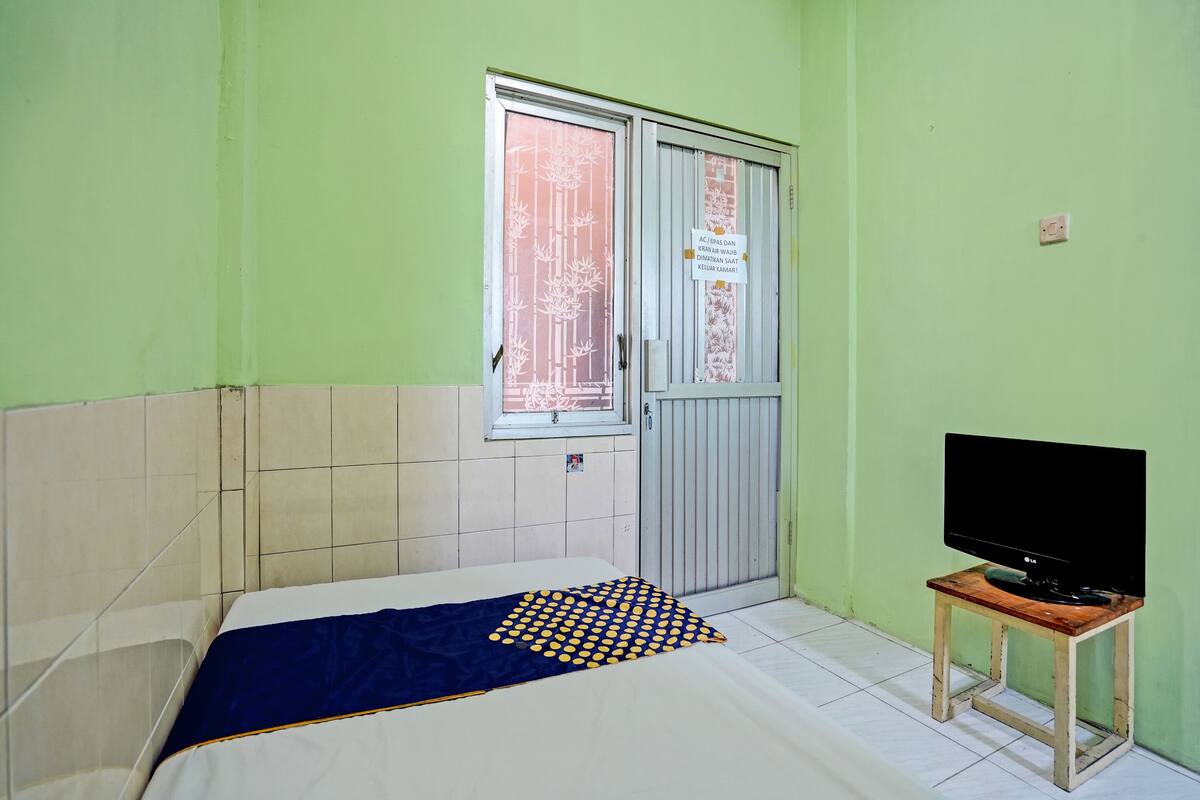 Ein Zimmer mit einem Bett, einem Fernseher auf einem Holzständer, einem Fenster mit Bambusmuster und einer Tür mit einem Schild.