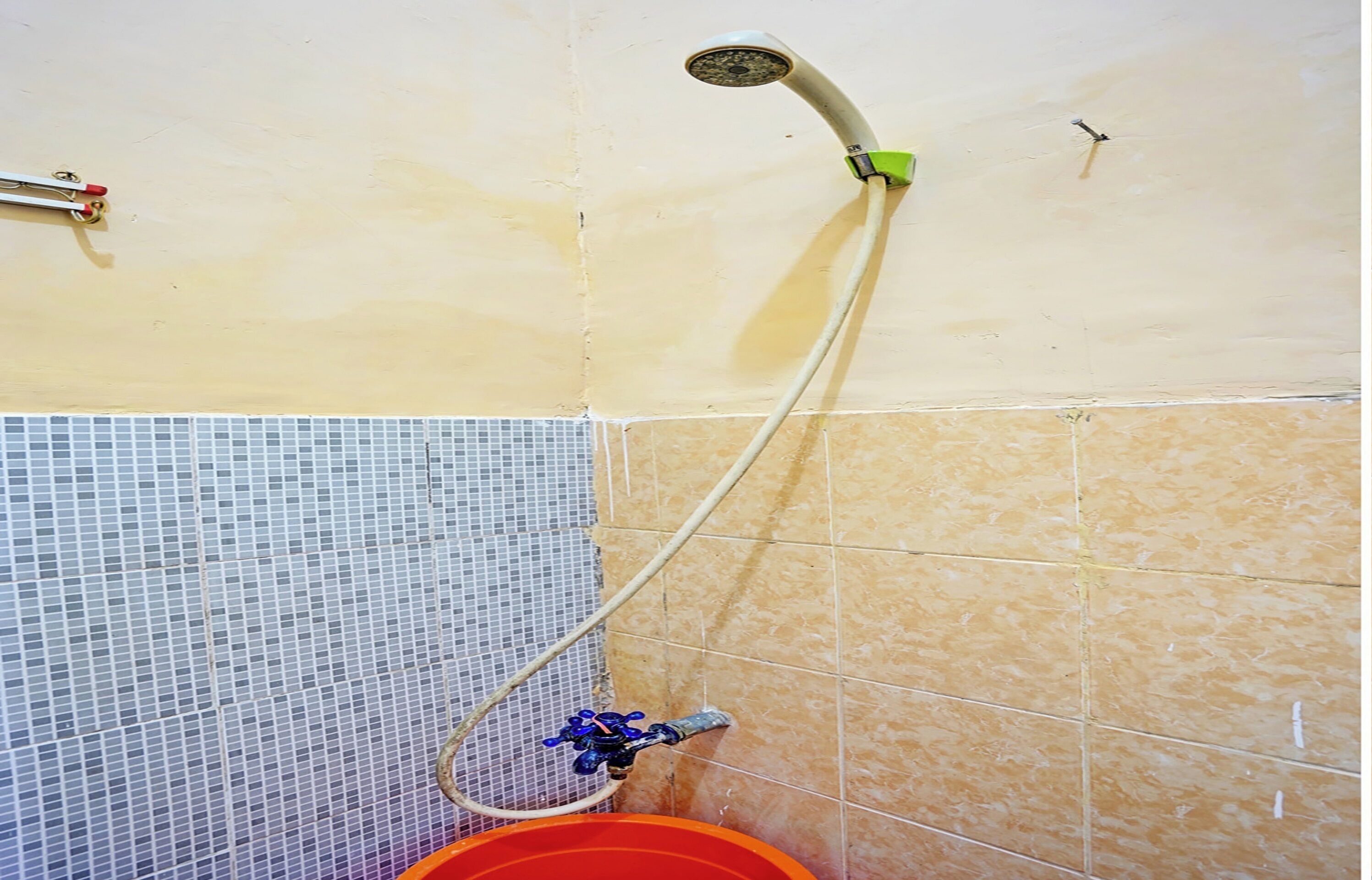 A shower with a hose, a red bucket, and a tiled wall.