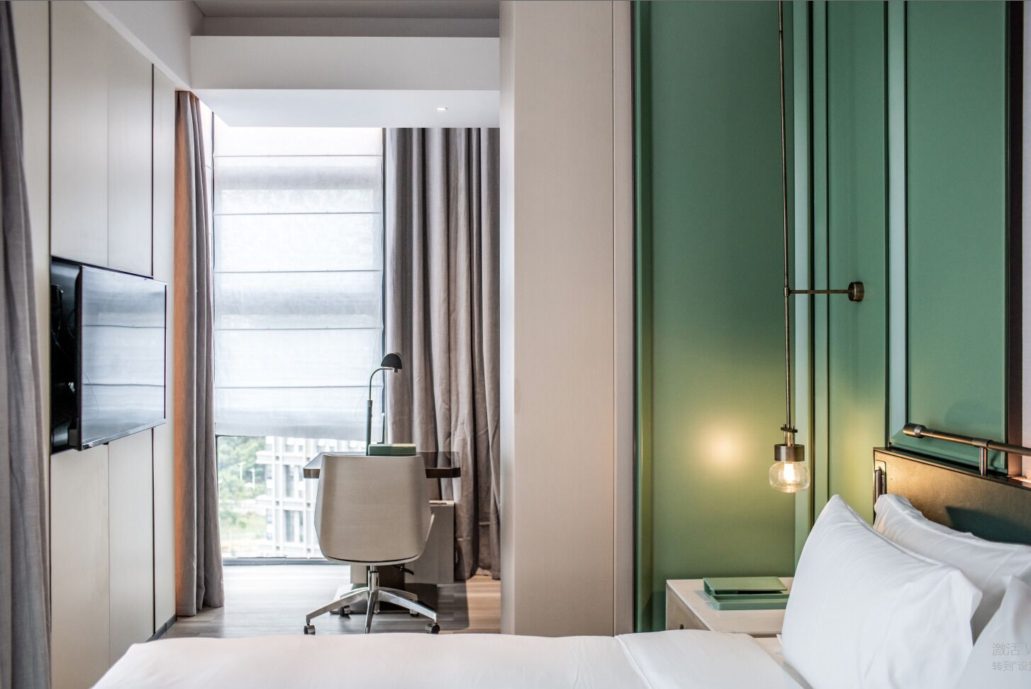 A modern hotel room with a bed, a desk, a chair, and a TV mounted on the wall.