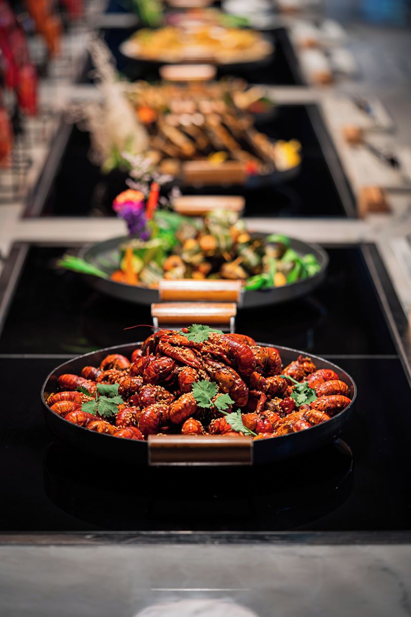 Una mesa de buffet con diversos platos, incluyendo una fuente destacada de langostas cocidas adornadas con hierbas.