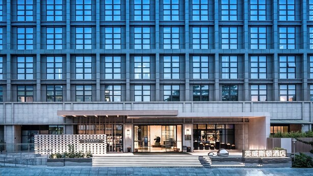 Un hôtel moderne doté d’une grande façade vitrée, d’une entrée imposante et d’un hall d’accueil bien éclairé.