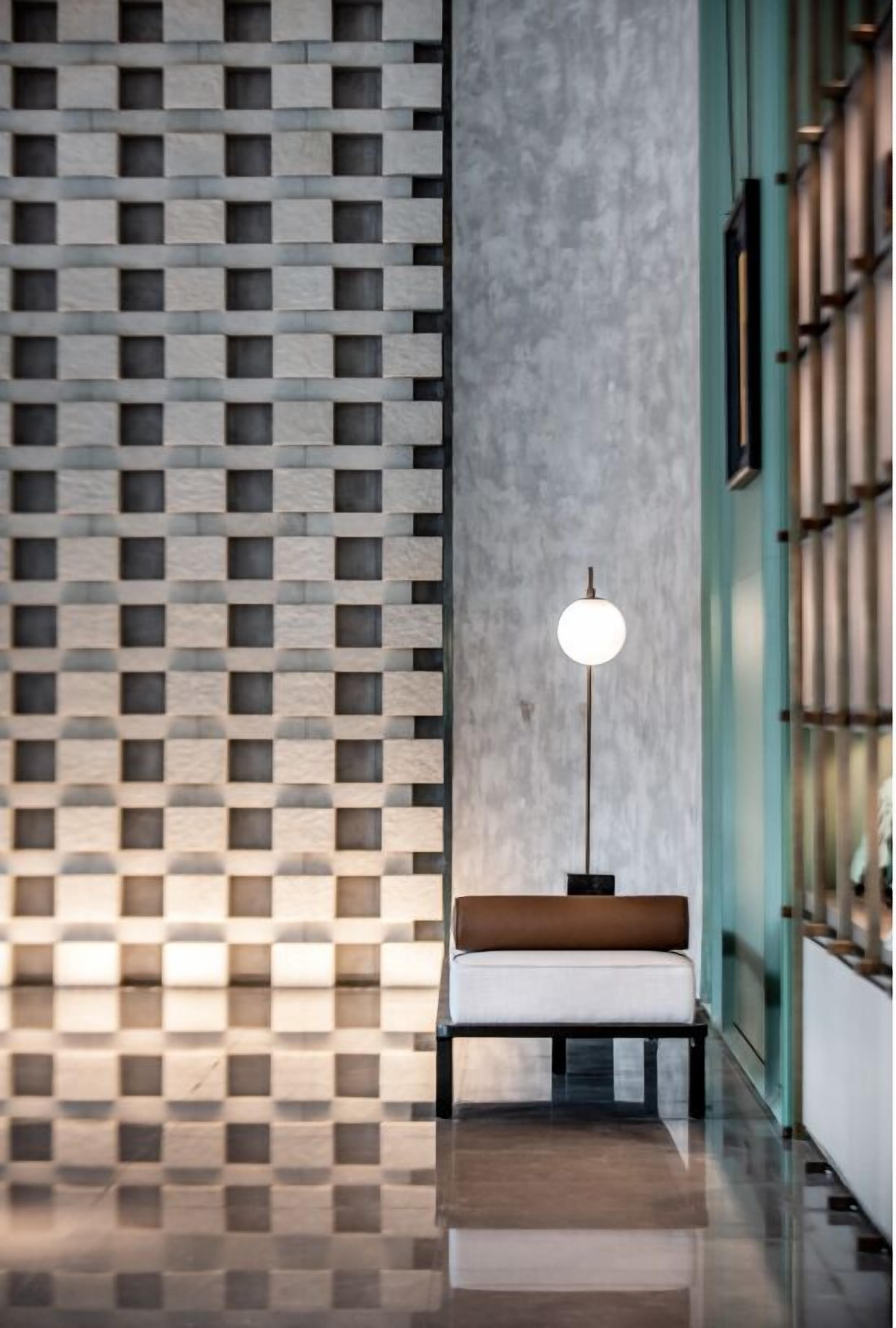 A modern interior with a checkered floor pattern, a bench with a light fixture, and a wall with a grid-like design.