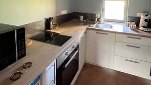 Cocina compacta con microondas, estufa, horno y lavabo. Una ventana proporciona luz natural.