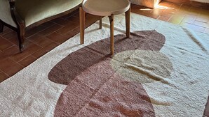 Una habitación con sofá, una mesita redonda, un tapete estampado y una ventana con luz natural.