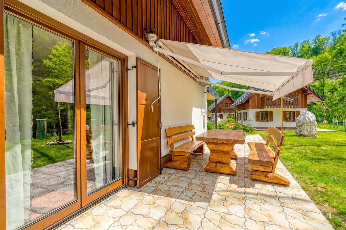 Eine Terrasse mit Holztisch und Bänken, ein überdachter Bereich mit weißem Baldachin und Blick auf eine bewaldete Landschaft.