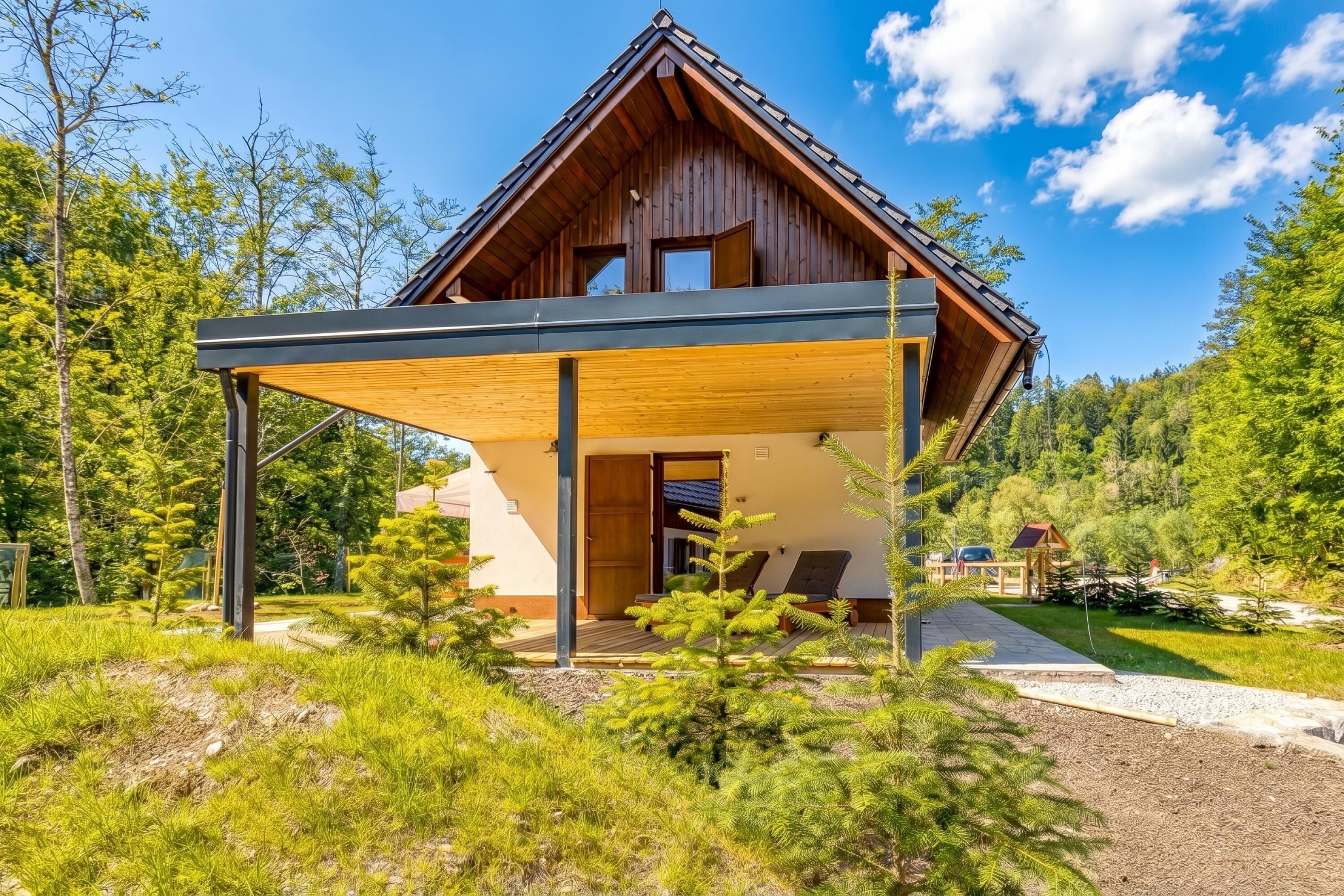A modern wooden cabin with a covered porch, surrounded by lush greenery and a clear sky.