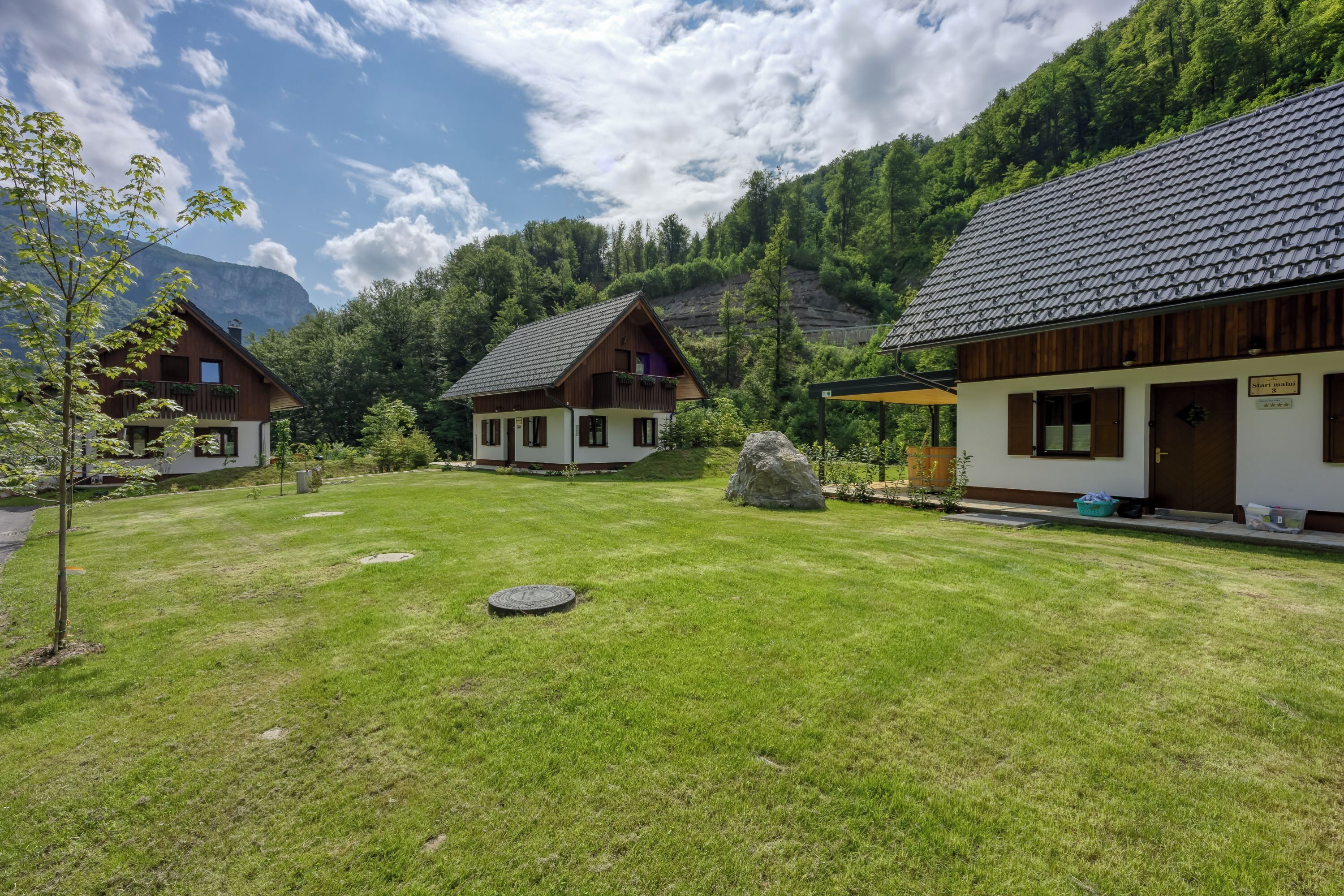 A mountain lodge with two main buildings, a grassy yard, and a large rock.